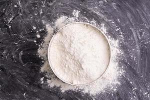 Flour in a bowl and wheat flour on table, black background In a rustic kitchen, top view photo