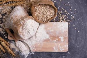 Flour and wheat grains in sacks with wheat ears On a black background table. In a rustic kitchen. Top view. photo