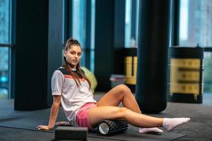 Young woman using a foam roller while doing stretching exercises photo