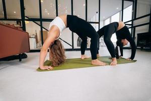 Two young woman practices bridge pose standing on a yoga mat. photo