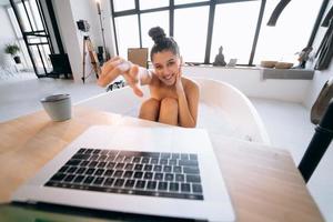 Young woman working on laptop while taking a bathtub photo