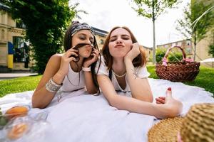 Two women having picnic together, laying on the park lawn photo