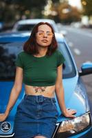 Beautiful girl sits on the hood of a blue car photo