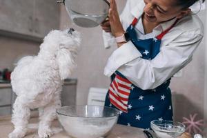 Woman in the kitchen sifts flour together with a dog photo