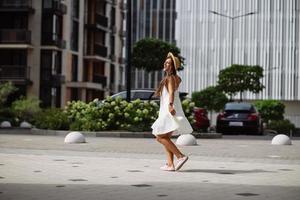 Beautiful pretty woman in white dress walking at city street photo