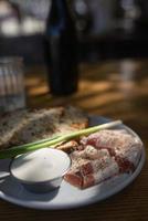 Close up view slices of smoked bacon meat with rye whole grain black bread, green onion and sour cream on the table. photo