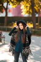 mujer elegante en poncho y sombrero disfruta del parque de otoño foto