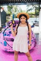 Young woman hose stands in front of a car covered in pink foam photo