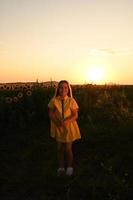 A happy young girl with long hair in a straw hat stands in a large field of sunflowers. Summer day. A warm sunset photo
