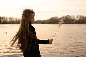 A girl with long hair on the shore of a lake. Standing in the wind and looking at a beautiful warm sunset. photo