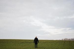 Teen boy wearing black jacket and white hat outside, enjoys in the early spring field.. photo