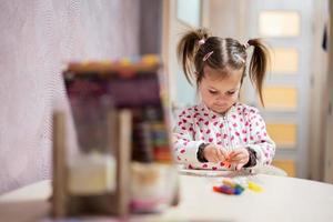 Baby girl with pigtails decorating art with glitter decor tube of paint. photo