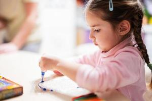 Little girl with pigtails decorating art with glitter decor tube of paint. photo