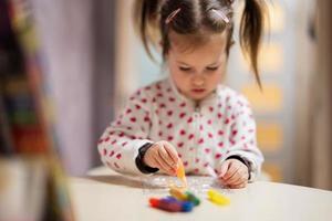 Baby girl with pigtails decorating art with glitter decor tube of paint. photo