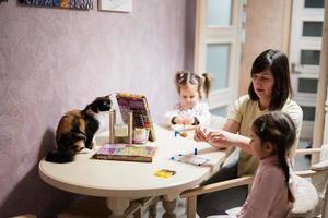 Mother and daughters decorating art with glitter decor. Also cat with them on table. photo