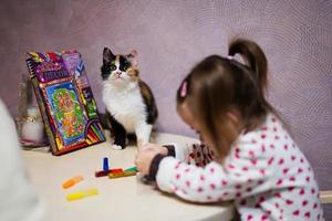 Baby girl with pigtails and cat decorating art with glitter decor tube of paint. photo