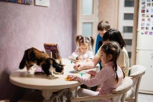 madre y niños decorando Arte con Brillantina decoración. además gato con ellos en mesa. foto