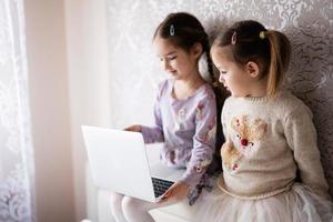 Two girls sisters watching on laptop. Technology and home concept. photo