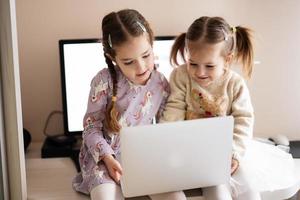dos muchachas hermanas acecho en ordenador portátil. tecnología y hogar concepto. foto