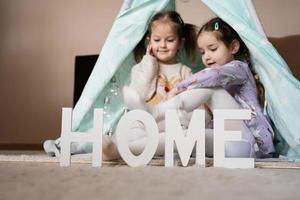 Two girls sisters at wigwam tent with wooden home letters. photo