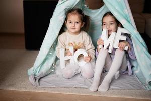 Two girls sisters at wigwam tent with wooden home letters. photo