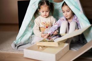 Two girls sisters at wigwam tent looking at parents wedding album. photo