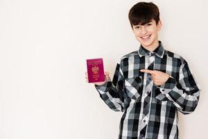 Young teenager boy holding Poland passport looking positive and happy standing and smiling with a confident smile against white background. photo