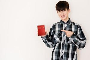 joven adolescente chico participación Suiza pasaporte mirando positivo y contento en pie y sonriente con un confidente sonrisa en contra blanco antecedentes. foto