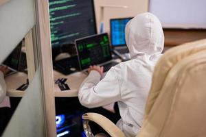 Boy hacker fraudulently use credit card for payment. Internet theft . Man wearing a balaclava and holding a credit card while sat behind a laptop. photo