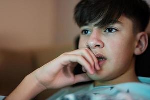 Young teen boy in front of a laptop on a bed at evening. photo