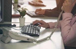 Businesswoman using white landline phone while working on computer at office workplace desk photo