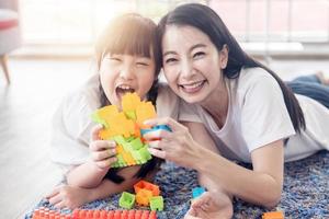 disfrutar contento amor asiático familia madre y pequeño linda niña sonriente jugando con juguete edificio o construcción juguetes a hogar foto