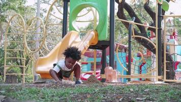 A cute African American boy playing sand in a sandbox area in playground