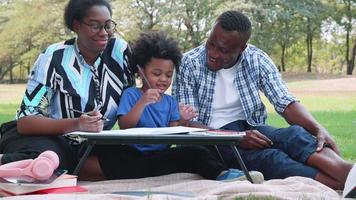 African American parents and child enjoy the picnic in park, and the son made homework video