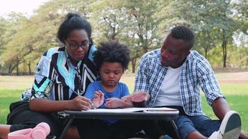 Happy African American Parents teach son to made homework in the park video