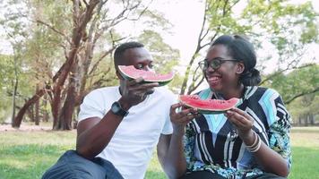 gelukkig Afrikaanse Amerikaans paar aan het eten vers watermeloen gedurende buiten datum in park video