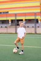 A teenage boy stands on a green field in the school yard with a soccer ball and looks away photo