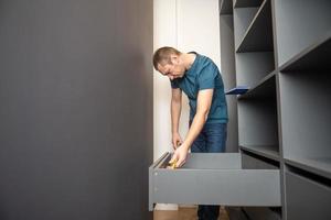 A young man collects furniture shelves in the closet according to the instructions photo