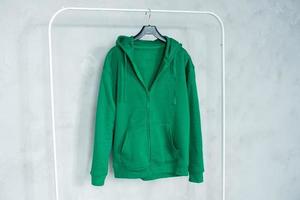 A set of layouts of a green hoodie with a zipper,a pocket, hanging on a hanger, holding in his hands, a sweatshirt with pleats. photo