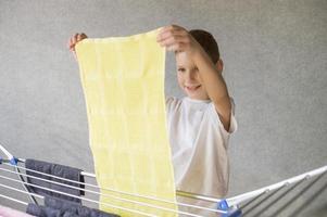 Cute boy hanging a wet towel on a metal clothes dryer, housework photo