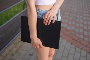 A girl holds a laptop in her hands against the background of her legs photo