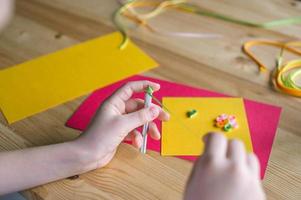 With the hands of a child, make a card out of quilling, twist a strip of narrow paper with an awl photo