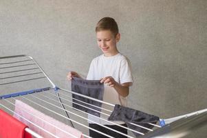 Cute boy doing household chores, hanging wet clothes on the dryer photo