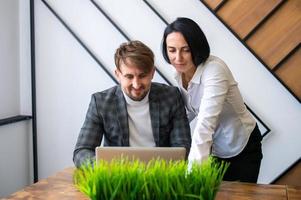 a woman stands next to a man sitting at a desk with a laptop in the office photo