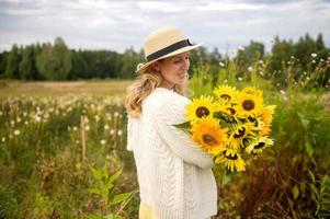 A cute girl in a hat with a brim holds a bouquet of sunflowers photo
