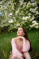 el niña es en pie debajo un árbol con su ojos cerrado. blanco pétalos son que cae en el cara foto