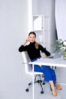 The girl works in a white office with a laptop and flowers on the table photo