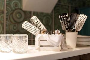 A set of hand graters stands near glasses and plates in the kitchen photo
