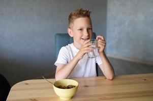 A cute boy drinks water and eats a dry breakfast at home and smiles photo