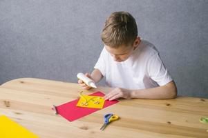 Cute child makes a card out of quilling, glue a strip of paper with white glue photo